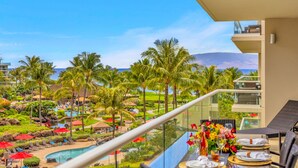 Un balcon offrant une vue sur une piscine d’un complexe hôtelier, des palmiers et une montagne en arrière-plan.