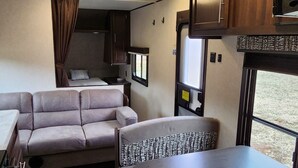 Un intérieur de camping-car compact comprenant un canapé, une table à manger, un coin cuisine et une fenêtre.