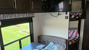 Un intérieur de camping-car compact comprenant un coin cuisine, une petite table à manger, un espace nuit et un téléviseur.