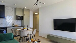 Una sala de estar moderna con un sofá verde, un comedor con una mesa dispuesta para dos personas, una cocina con microondas y un televisor grande montado en la pared.