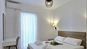 Una habitación de hotel con cama, escritorio, silla, mesita de noche y lámpara de pared.