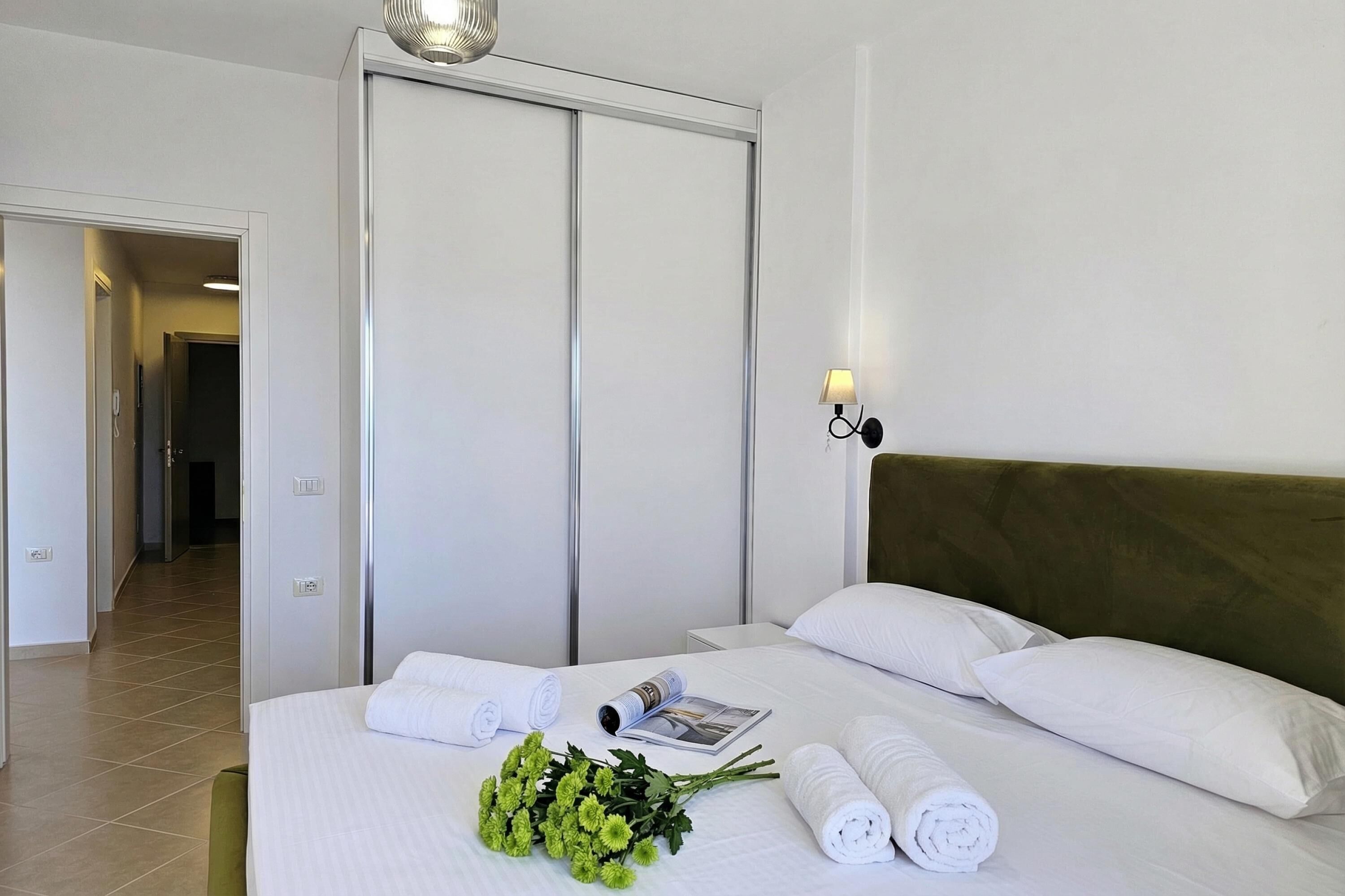 Ein Hotelzimmer mit Bett, Nachttisch, Lampe, Tür und Flur.