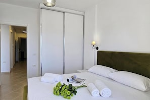 A hotel room with a bed, a nightstand, a lamp, a door, and a hallway. - Ionian Blue Escape 304 /w Sea View Balcony, Sarandë, Albania (Sarandë)