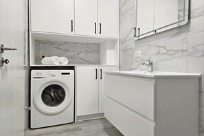 A modern laundry room with a front-loading washing machine, white cabinets, and a marble-tiled wall. - Ionian Blue Escape 304 /w Sea View Balcony, Sarandë, Albania (Sarandë)