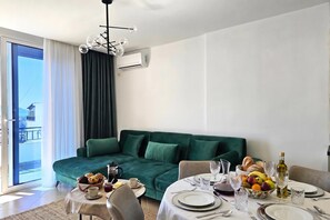 A modern living room with a green sofa, a dining table set for two, and a balcony with a view. - Ionian Blue Escape 304 /w Sea View Balcony, Sarandë, Albania (Sarandë)