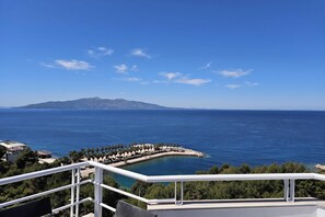 A coastal view with a clear sky, a beach with palm trees, and a distant mountain. - Two Bedroom Apartment With Sea View-061, Sarandë, Albania (Sarandë)