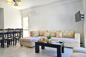 Ein Wohnzimmer mit einer Couch, einem Couchtisch, einem Esstisch mit Stühlen und einem an der Wand befestigten Fernseher.