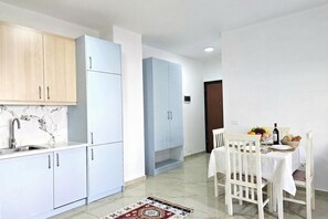 A modern kitchen with white cabinets, a marble backsplash, and a dining area with a table set for two. - One Bedroom Apartment In Saranda - 001, Sarandë, Albania (Sarandë)