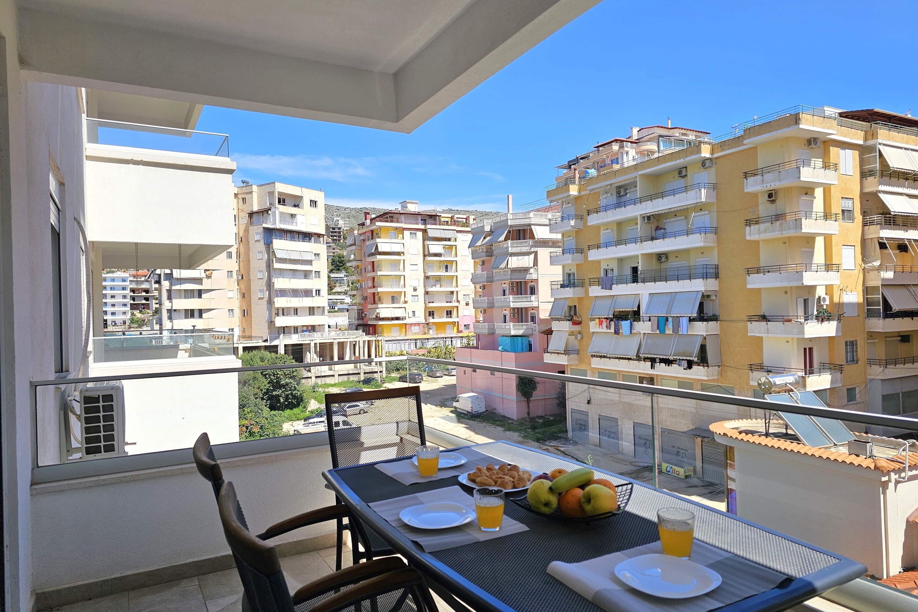 A balcony with a table set for two, a chair, and a view of surrounding buildings.