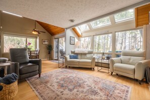 A spacious living room with a ceiling fan, large windows, a fireplace, and a cozy seating area. - Lakefront Condo, Dock/Fire Pit, Walk to Honi/Uno (Oakland)