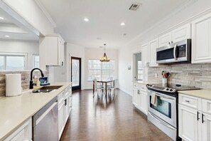 Una cocina moderna con armarios blancos, un microondas de acero inoxidable y una isla grande con un lavamanos.