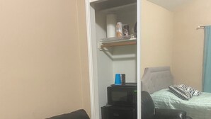 Een kamer met een zwarte leren bank, een spiegelende kastdeur, een bed met een gestreept kussen en een kleine zwarte tafel met een blauwe beker.