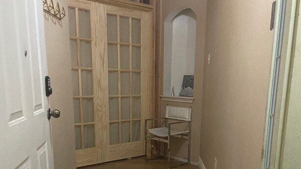 Een smalle gang met houten vloer, een witte deur, een zwart voetenbankje, een houten kast en een spiegel aan de muur.