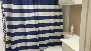 Een badkamer met een gordijn met strepen, een wit toilet en een witte wastafel.
