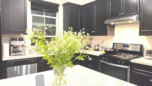 Une cuisine avec des meubles de couleur sombre, une machine à café, une cuisinière et un vase rempli de fleurs posé sur le comptoir.