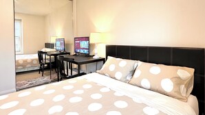 Une chambre à coucher avec un lit, deux écrans d’ordinateur, un bureau et une chaise.
