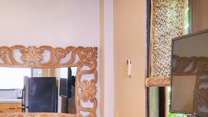 A room with a wooden vanity, a mirror with ornate carvings, a small stool, and a window with a view of greenery.