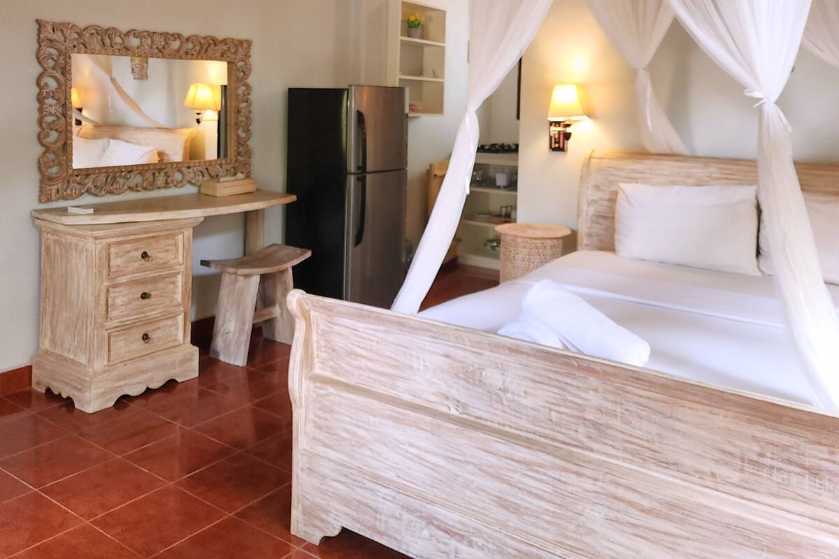 Une chambre à coucher avec un lit à baldaquin, une commode en bois, un miroir, un réfrigérateur et une horloge murale.