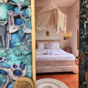 A bedroom with a canopy bed, a Buddha statue, and a wall-mounted lamp. - Danaya Cottage Ubud (Ubud)