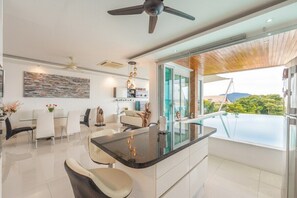 A modern kitchen with a glass island, dining area with chairs, and a view of the outdoors. - Seaview Rooftop Pool Villa Near Beach V210 (Rawai)