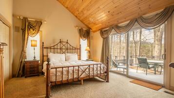 A bedroom with a wooden bed, a nightstand, a lamp, and a view of the outdoors through a sliding glass door.