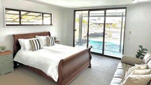 Ein Schlafzimmer mit Bett, Sofa, Fenster und Blick auf einen Swimmingpool.