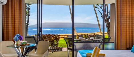 A hotel room with a large sliding glass door leading to a balcony with a view of the ocean and a grassy area.