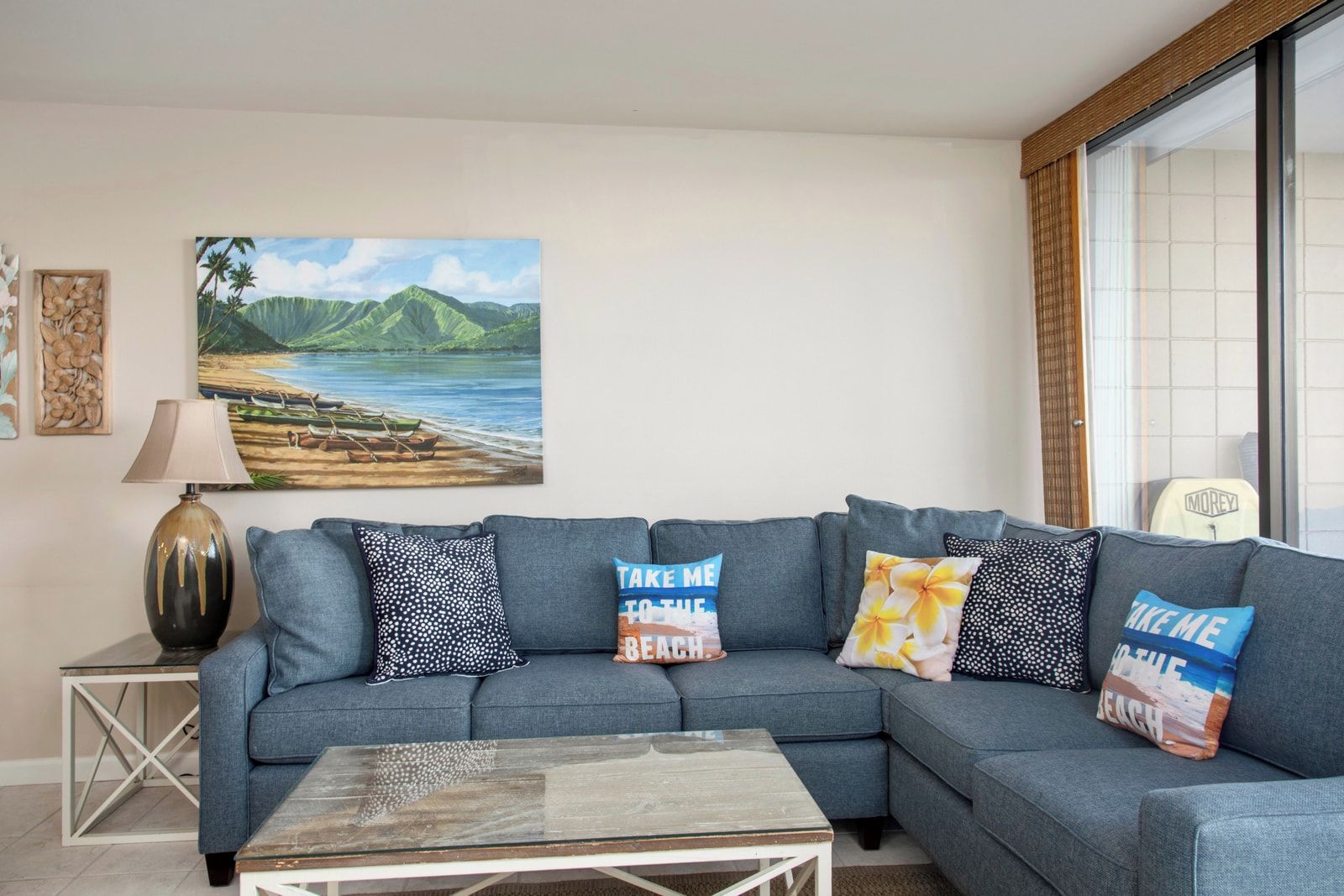 A living room with a grey sofa, a coffee table, a painting of a beach, and a lamp.