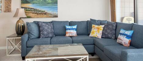 A living room with a grey sofa, a coffee table, a painting of a beach, and a lamp.