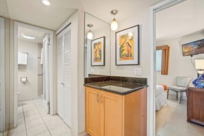 Een badkamer met een douche, toilet en wastafel. Er hangen afbeeldingen in lijsten aan de muur, een plafondlamp en een raam met gordijnen.