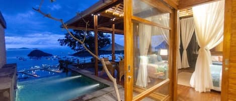 Eine Holzterrasse mit Pool, die auf einen Yachthafen bei Nacht blickt.