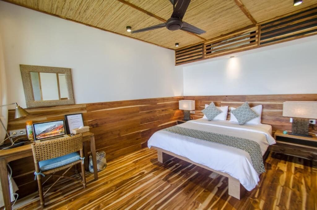 Um quarto com painéis de madeira, uma cama, uma escrivaninha e um ventilador de teto.