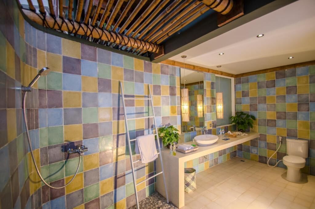 A bathroom with a tiled wall, a shower, a sink, a toilet, and a mirror.