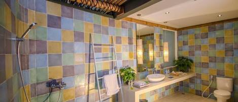 A bathroom with a tiled wall, a shower, a sink, a toilet, and a mirror.