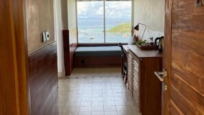 Passadís estret que condueix a una habitació amb una finestra gran, una banca i una porta de fusta.