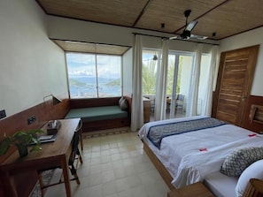 Una habitación con cama, escritorio, ventana con vistas y ventilador de techo.