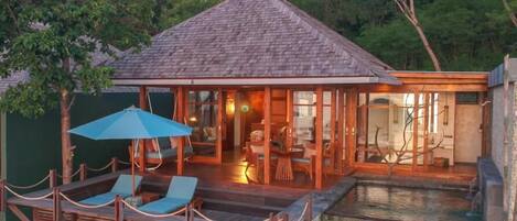 A wooden house with a tiled roof, a pool, and a deck with lounge chairs and an umbrella.