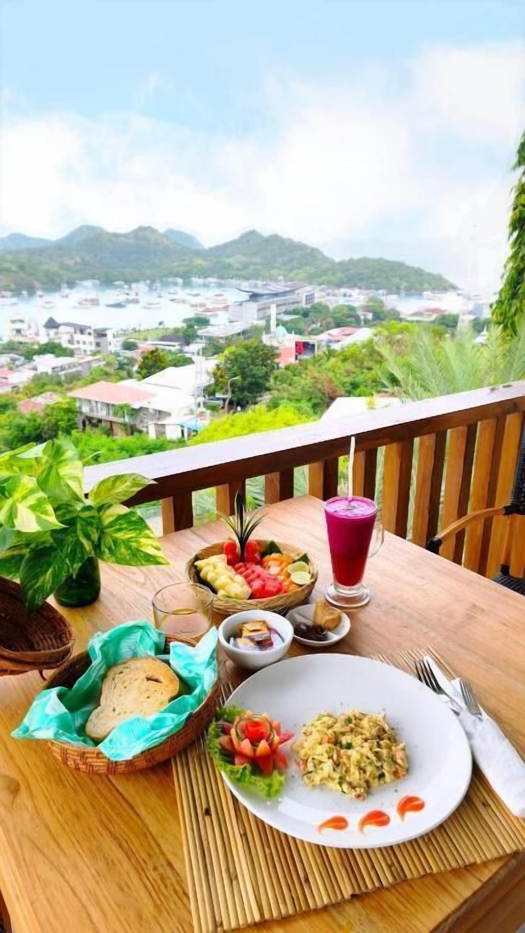 Une table dressée avec de la nourriture et des boissons sur un balcon donnant sur une ville et des montagnes.