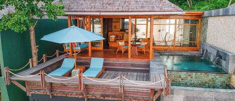 A wooden deck with lounge chairs and a table, a glass-enclosed room with a view, and a small pool.