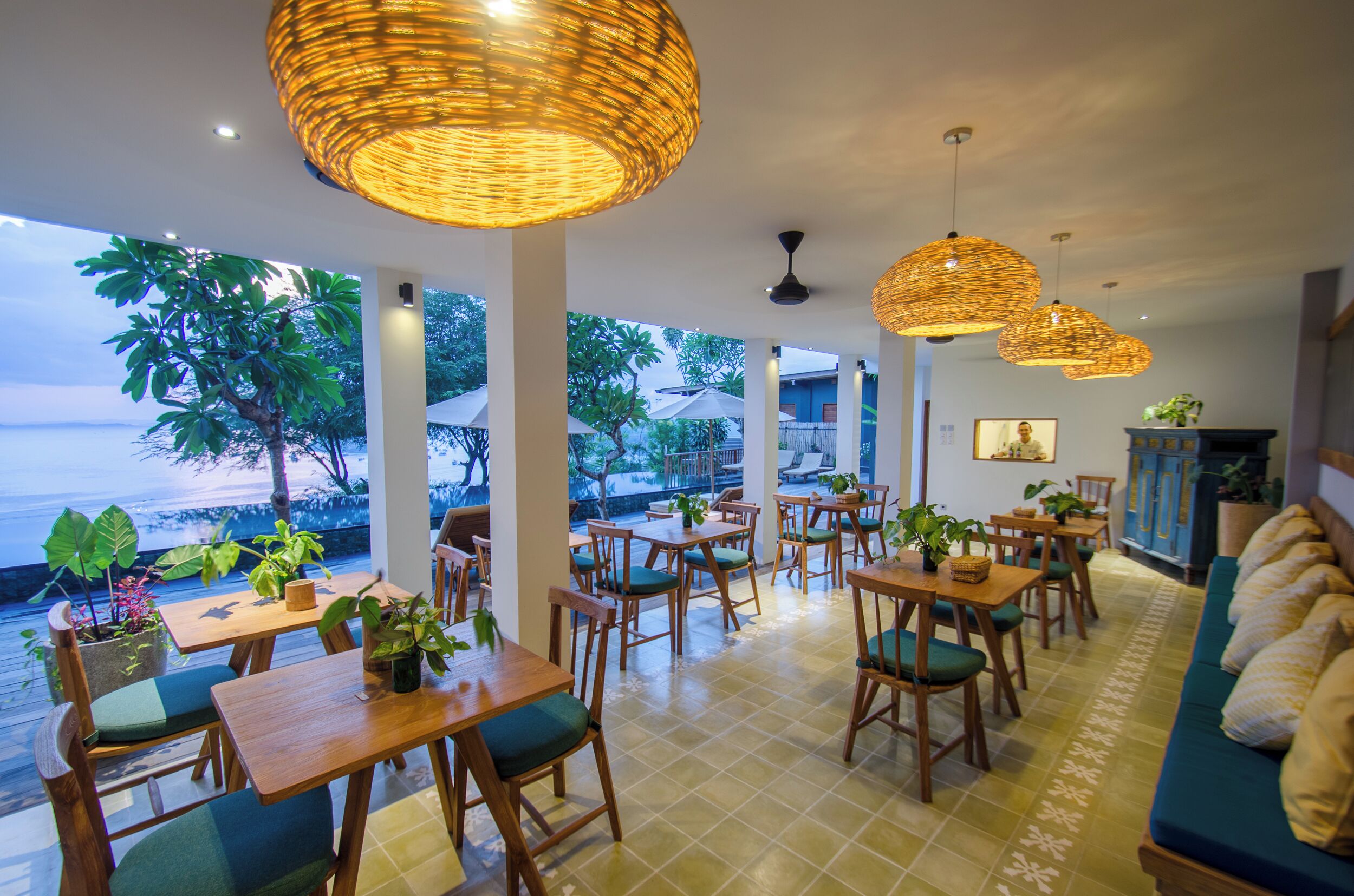 Un restaurante con mesas y sillas de madera, lámparas de mimbre colgantes y vista al océano.