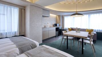 Una camera d'albergo con un letto, un tavolo da pranzo con sedie, un angolo cottura e un'ampia finestra con tende.