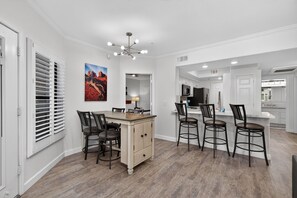 A modern kitchen with white cabinetry, a dining area with a wooden table and chairs, and a large painting on the wall. - Spacious 2BR 2BA Condo Getaway for 6 (Scottsdale)