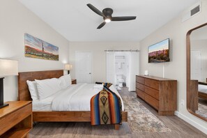 A bedroom with a bed, a wooden dresser, a ceiling fan, a TV, and artwork on the walls. - Spacious 2BR 2BA Condo Getaway for 6 (Scottsdale)