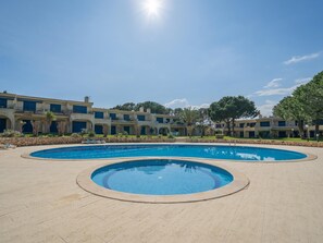 A pool area with two circular pools and a building with multiple balconies in the background. - Pool retreat at Clube da Bemposta (Alvor)