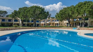 Una piscina con un muro de piedra y un edificio con balcones al fondo.