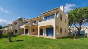 Un edificio de varios pisos con balcones, arcos en las entradas y un césped bien cuidado.
