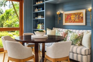 A room with a round table, chairs, a sofa, a bookshelf, and a painting. - Kapalua Bay Resort | Ocean View 6 BR | Car Incl. w/ 6+ Nights | MON ML-3818 by KBM (Lahaina)