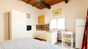 Une cuisine compacte avec un îlot central, un coin repas avec une chaise, un lit et une horloge au mur.