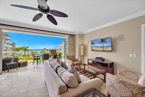 Ein modernes Wohnzimmer mit einer großen Couch, einem Couchtisch, einem Fernseher und einem Balkon mit Blick auf das Meer und Gebäude.