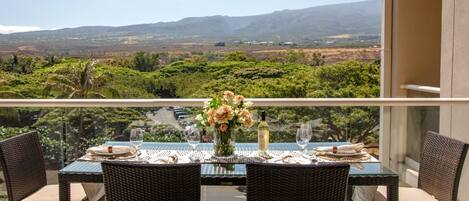 Un comedor con una mesa lista para dos personas, con vistas a un paisaje pintoresco con montañas y follaje.